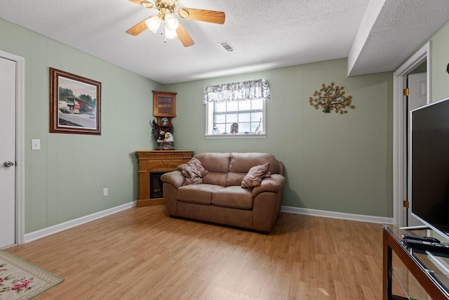 living area featuring light wood-type flooring, ceiling fan, visible vents, and a textured ceiling