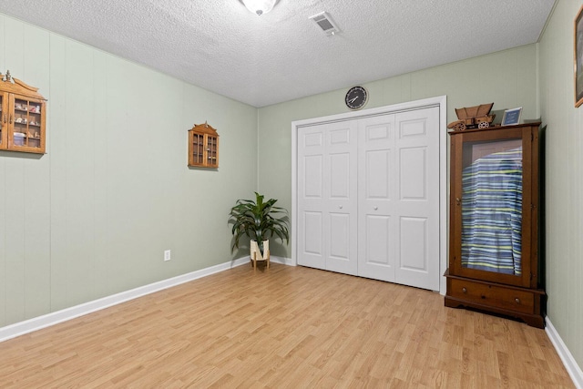 unfurnished bedroom featuring a textured ceiling, visible vents, baseboards, a closet, and light wood-type flooring