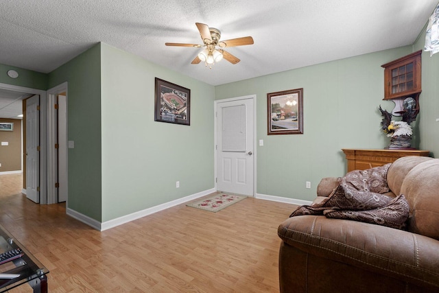 living area featuring light wood-type flooring, ceiling fan, a textured ceiling, and baseboards