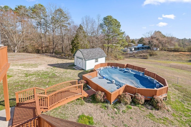 view of pool with a wooden deck, an outbuilding, fence, a storage unit, and a yard