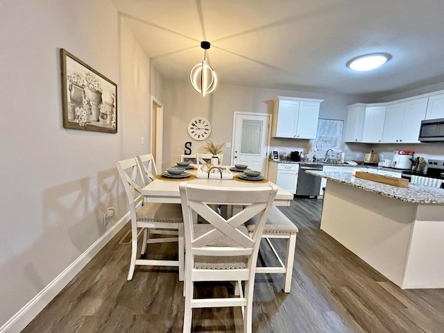 kitchen with dark wood-type flooring, a sink, appliances with stainless steel finishes, white cabinets, and baseboards