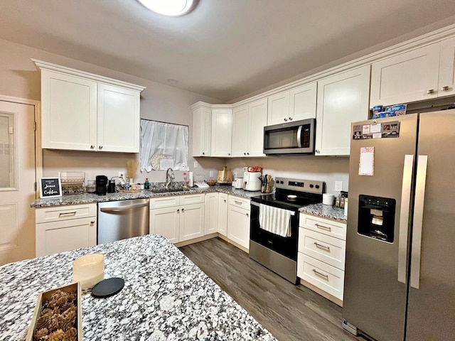 kitchen featuring dark wood-type flooring, light stone countertops, appliances with stainless steel finishes, white cabinets, and a sink