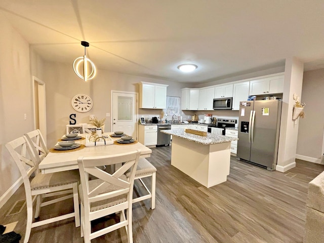 kitchen with a sink, wood finished floors, a center island, appliances with stainless steel finishes, and white cabinets