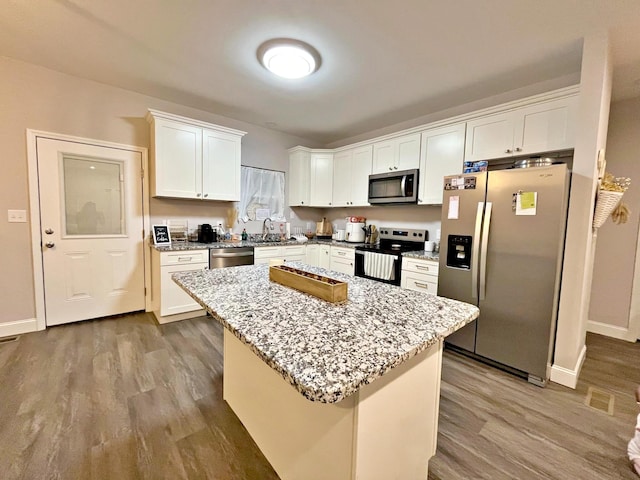kitchen with light stone countertops, wood finished floors, a kitchen island, white cabinets, and appliances with stainless steel finishes