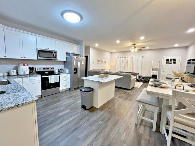 kitchen featuring light stone counters, a center island, light wood-style floors, appliances with stainless steel finishes, and ceiling fan