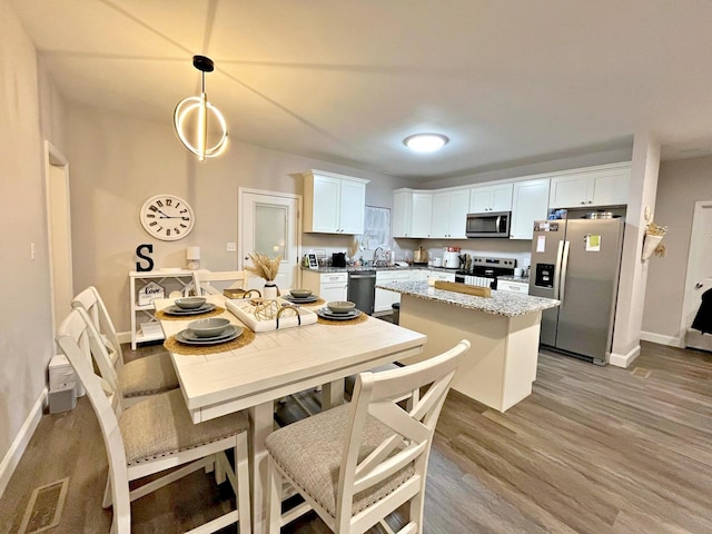kitchen featuring a center island, light wood-style floors, white cabinets, stainless steel appliances, and a sink