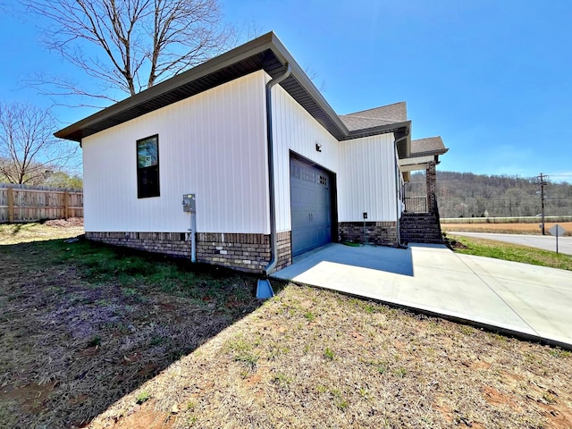 view of property exterior featuring concrete driveway, an attached garage, and fence