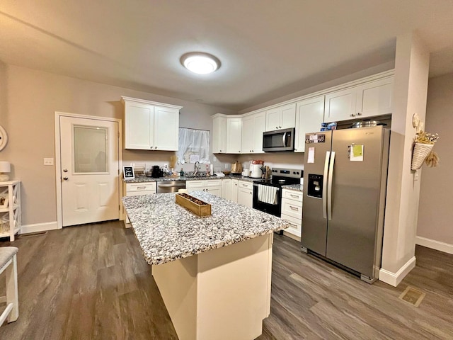 kitchen featuring dark wood-type flooring, light stone countertops, appliances with stainless steel finishes, white cabinets, and a sink