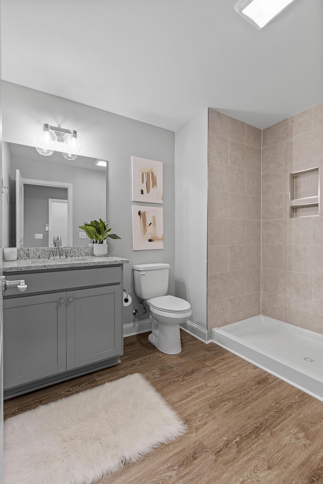 full bath featuring baseboards, toilet, wood finished floors, a tile shower, and vanity