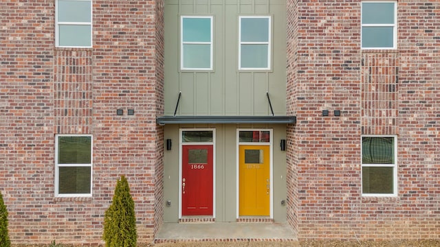 doorway to property featuring board and batten siding, a standing seam roof, brick siding, and metal roof