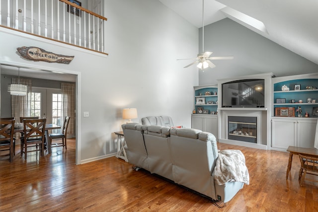 living room with baseboards, ceiling fan, french doors, a glass covered fireplace, and wood-type flooring