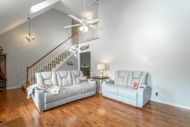 living area featuring baseboards, stairway, ceiling fan with notable chandelier, a skylight, and wood finished floors