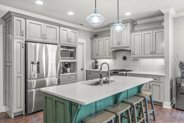 kitchen featuring a kitchen bar, sink, hanging light fixtures, stainless steel appliances, and a kitchen island with sink