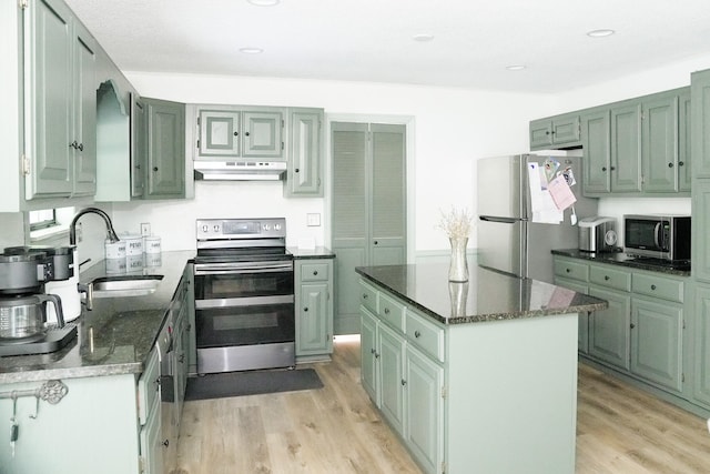 kitchen with sink, light hardwood / wood-style flooring, dark stone countertops, a kitchen island, and appliances with stainless steel finishes