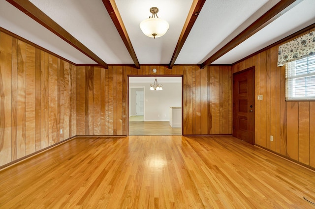 spare room featuring beam ceiling, light wood-type flooring, a notable chandelier, and wood walls