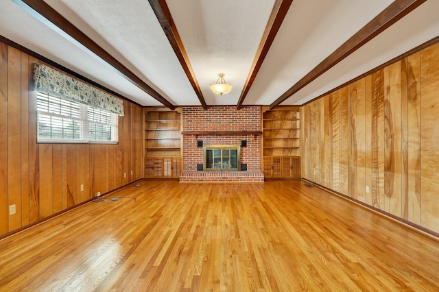 unfurnished living room with wood walls, light wood-type flooring, built in features, a fireplace, and beamed ceiling