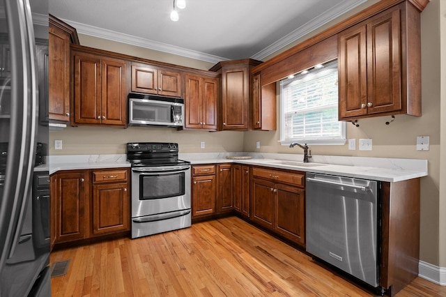 kitchen with ornamental molding, visible vents, appliances with stainless steel finishes, a sink, and light wood finished floors