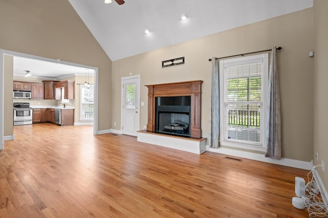 unfurnished living room with a wealth of natural light, high vaulted ceiling, and light wood-style floors