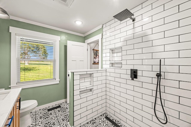 full bath featuring toilet, vanity, baseboards, visible vents, and tiled shower