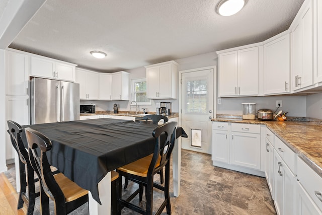 kitchen with white cabinets, light stone counters, a textured ceiling, and stainless steel refrigerator