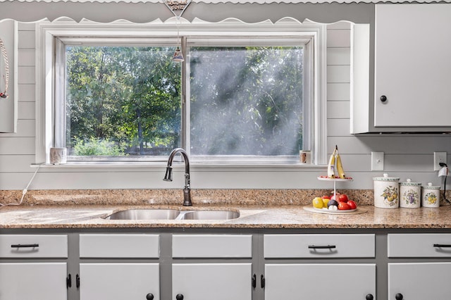 kitchen featuring light stone countertops, white cabinetry, and sink