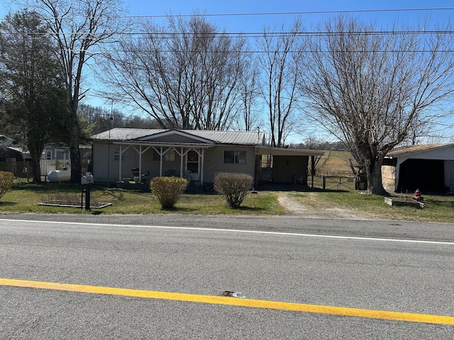 view of front facade with an attached carport, dirt driveway, fence, a front yard, and metal roof