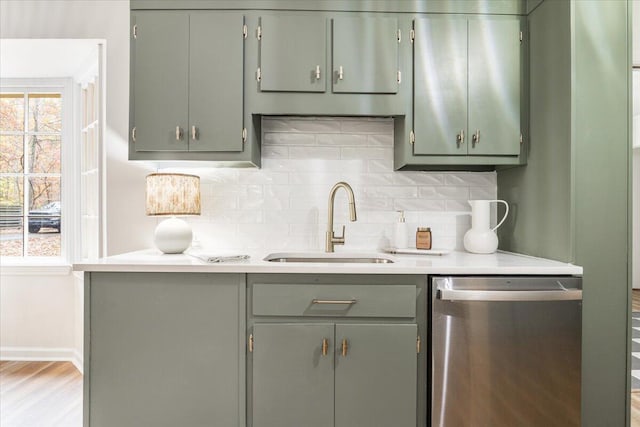 kitchen with dishwasher, sink, green cabinetry, light wood-type flooring, and tasteful backsplash