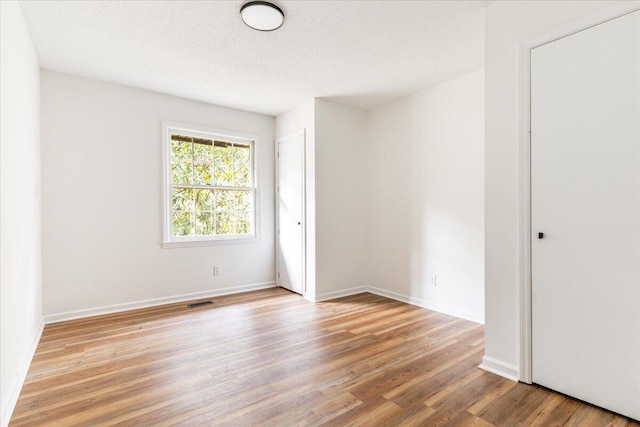 spare room with a textured ceiling and light hardwood / wood-style floors