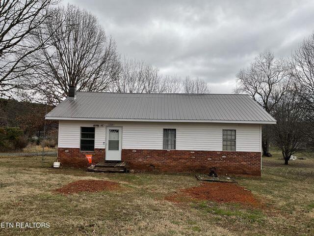 view of front of house with metal roof, brick siding, a chimney, and a front yard