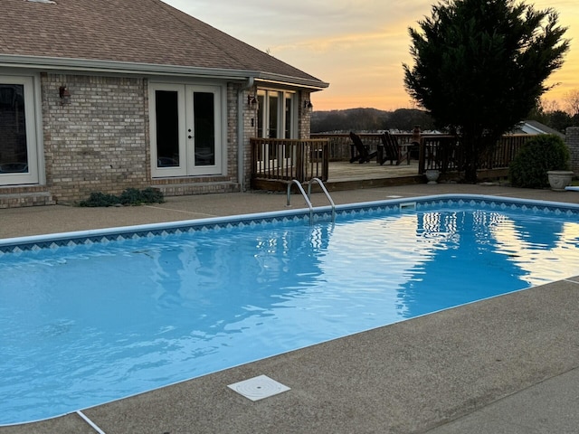 pool at dusk featuring a wooden deck and french doors