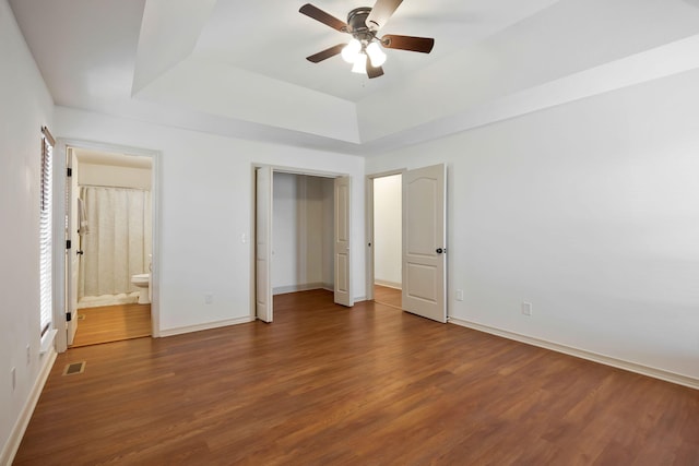 unfurnished bedroom featuring ceiling fan, dark hardwood / wood-style flooring, a tray ceiling, and connected bathroom