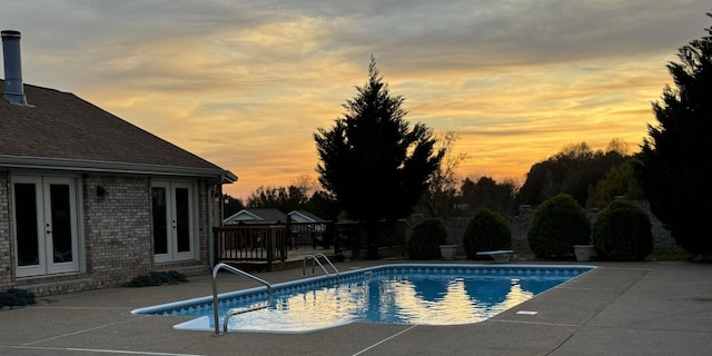 pool at dusk with a patio area and french doors