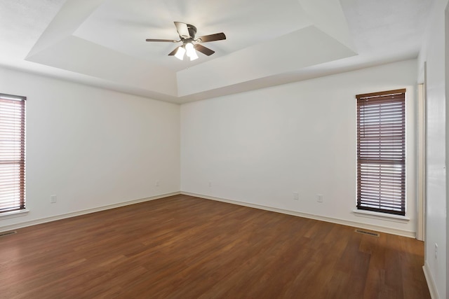 unfurnished room featuring ceiling fan, dark hardwood / wood-style floors, and a tray ceiling