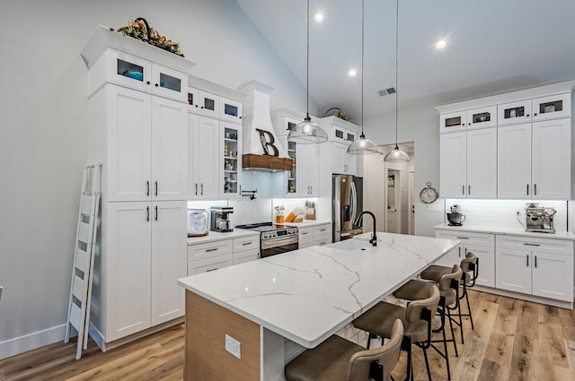 kitchen with white cabinetry, a center island with sink, decorative light fixtures, and appliances with stainless steel finishes