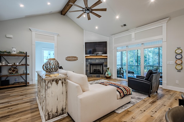 living room featuring high vaulted ceiling, a tile fireplace, ceiling fan, beamed ceiling, and light hardwood / wood-style floors