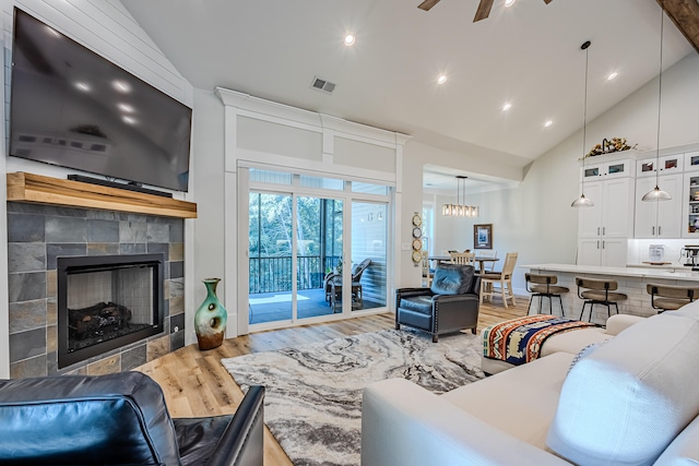 living room featuring high vaulted ceiling, ceiling fan, light wood-type flooring, and a tile fireplace