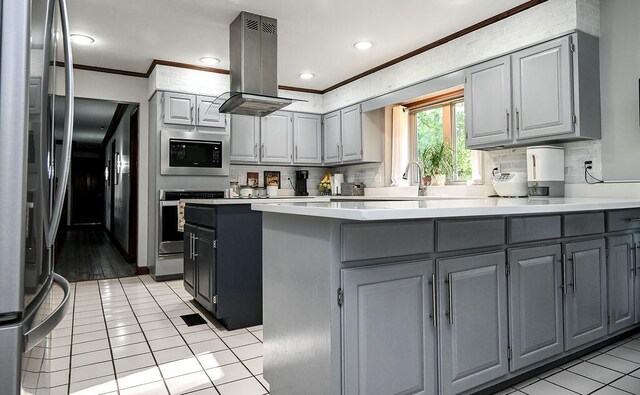 kitchen with gray cabinetry, island range hood, stainless steel appliances, crown molding, and light tile patterned floors