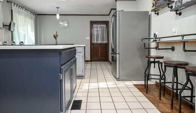 kitchen featuring hanging light fixtures, light tile patterned floors, ornamental molding, a breakfast bar area, and stainless steel refrigerator