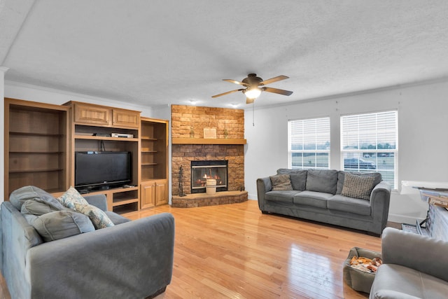 living room featuring light wood-style flooring, ornamental molding, a textured ceiling, a fireplace, and ceiling fan