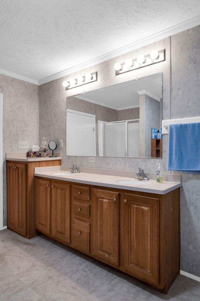 full bath featuring a sink, a textured ceiling, a shower stall, crown molding, and double vanity