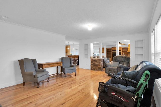 sitting room with light wood-type flooring, built in shelves, a textured ceiling, crown molding, and baseboards