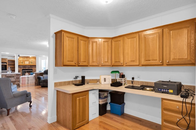 office area featuring ornamental molding, a ceiling fan, a textured ceiling, a large fireplace, and light wood finished floors