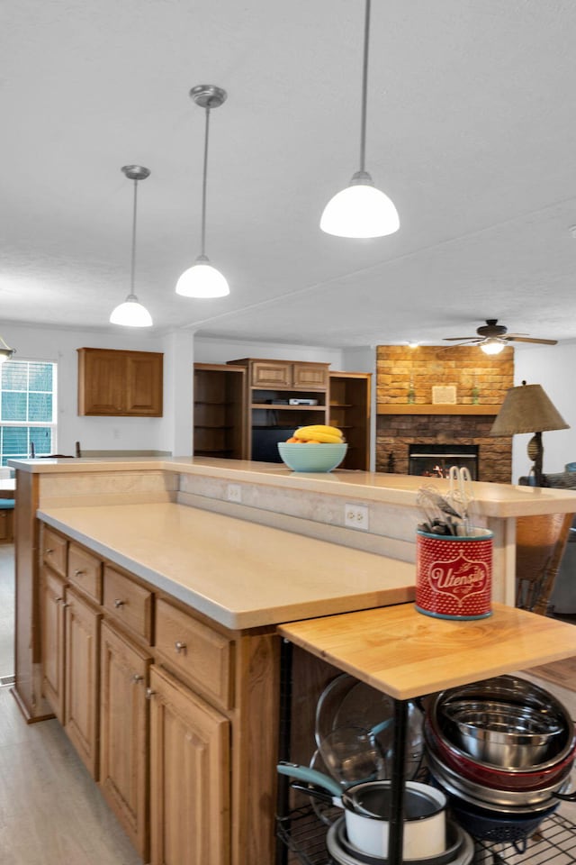 kitchen featuring a kitchen island, a stone fireplace, light wood-style flooring, and light countertops