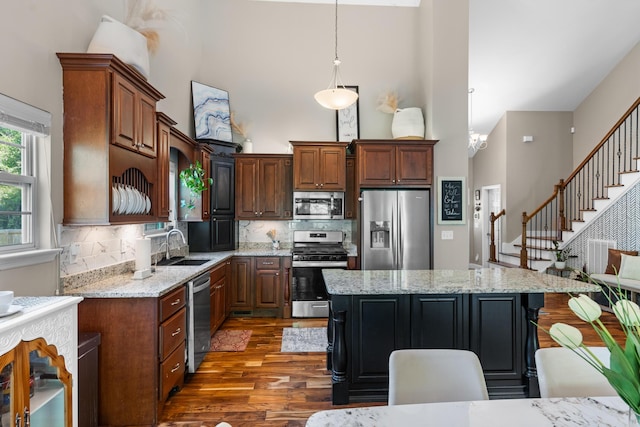 kitchen with a sink, appliances with stainless steel finishes, wood finished floors, and a towering ceiling
