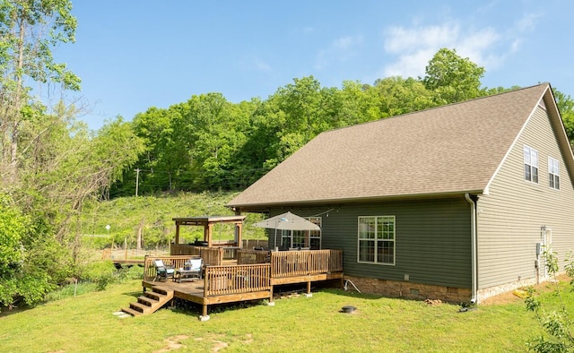 rear view of property featuring roof with shingles, a wooden deck, and a yard
