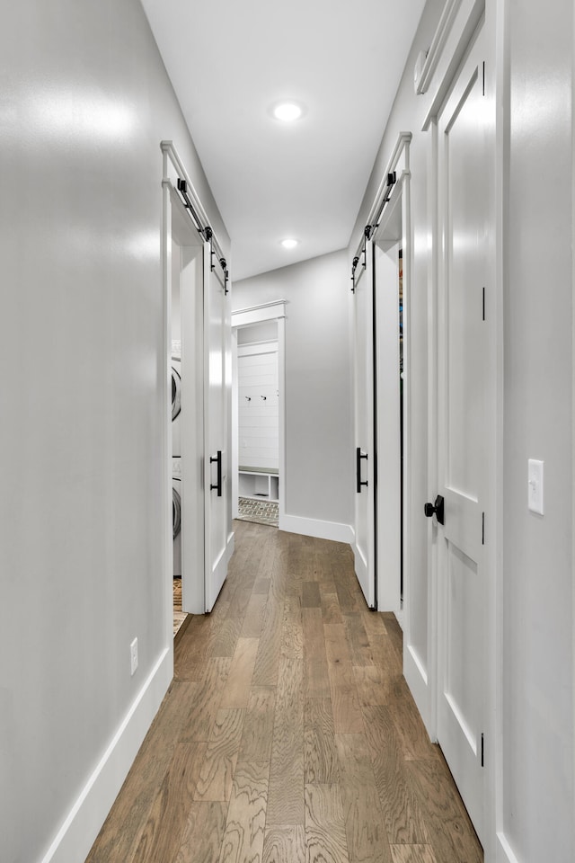 corridor with hardwood / wood-style flooring, a barn door, and stacked washer and clothes dryer