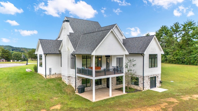 rear view of house featuring a lawn, a balcony, and a patio