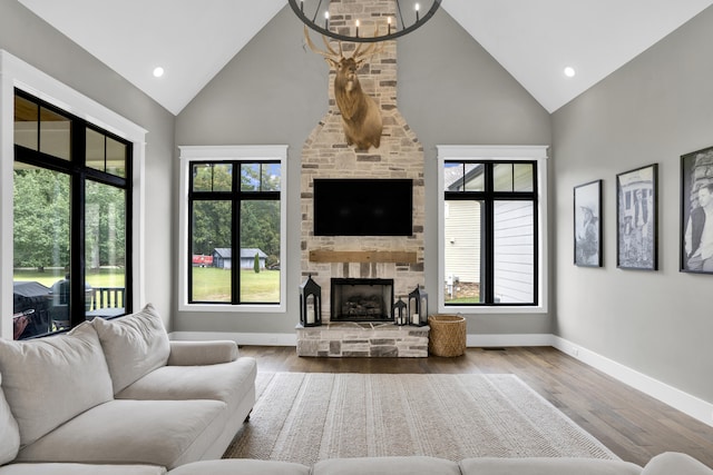 living room with a stone fireplace, hardwood / wood-style floors, high vaulted ceiling, and an inviting chandelier