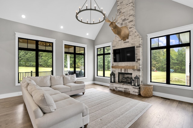 living room with a stone fireplace, hardwood / wood-style floors, high vaulted ceiling, and a chandelier