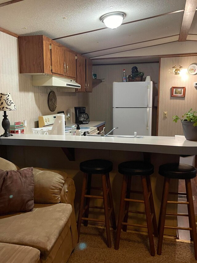 kitchen with a kitchen bar, sink, a textured ceiling, and white appliances